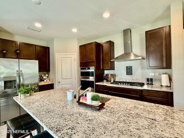 195 Torres Trce, Saint Augustine, FL 32095 - kitchen with wall chimney exhaust hood, stainless steel appliances, a kitchen bar, dark brown cabinetry, and light stone countertops