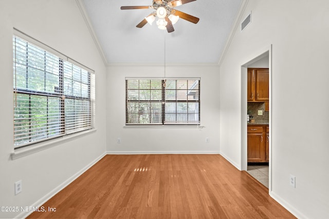 unfurnished room with crown molding, light wood-style floors, a ceiling fan, vaulted ceiling, and baseboards