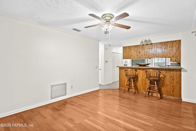 kitchen featuring brown cabinetry, crown molding, a ceiling fan, light wood finished floors, and a kitchen breakfast bar
