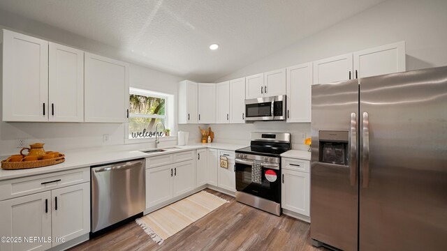 kitchen featuring stainless steel appliances, a sink, light countertops, white cabinetry, and lofted ceiling