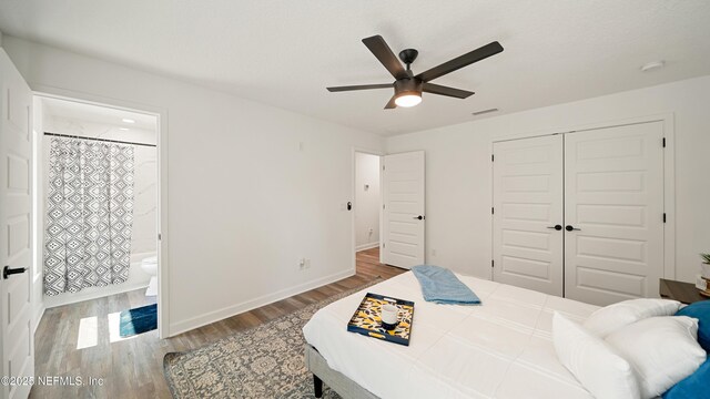 bedroom with wood finished floors, a closet, a ceiling fan, ensuite bathroom, and baseboards