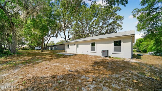 back of property with central AC, stucco siding, and metal roof