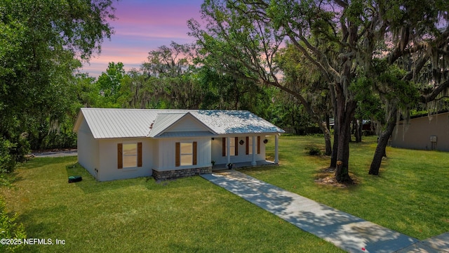 ranch-style house featuring concrete driveway, a yard, a porch, metal roof, and stucco siding