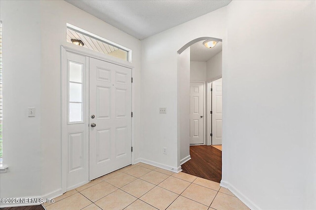 foyer featuring arched walkways, baseboards, and light tile patterned floors