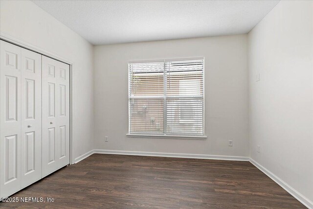 unfurnished bedroom with dark wood finished floors, baseboards, and a closet