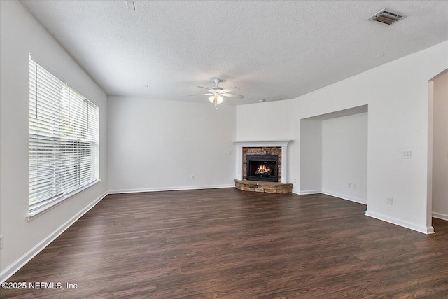 unfurnished living room with ceiling fan, a textured ceiling, dark wood finished floors, a fireplace, and baseboards