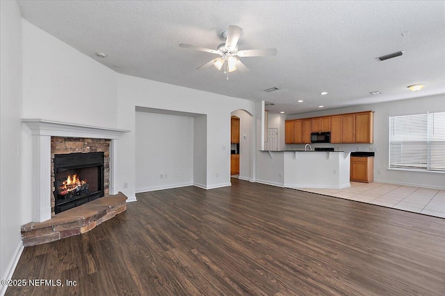 unfurnished living room featuring light wood-style floors, ceiling fan, arched walkways, baseboards, and a fireplace