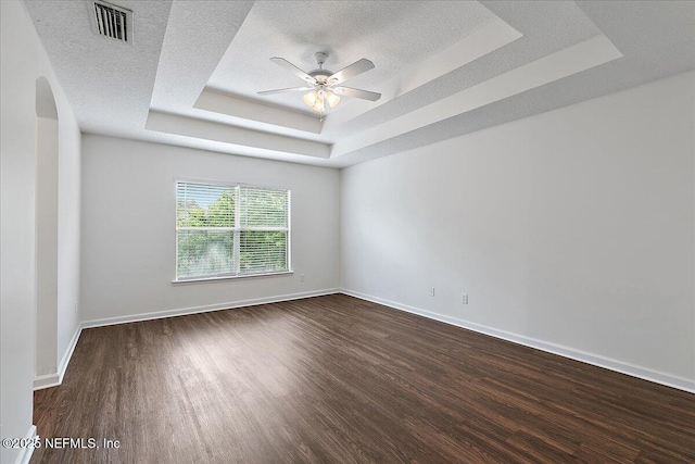 unfurnished room featuring a tray ceiling, arched walkways, wood finished floors, a ceiling fan, and baseboards