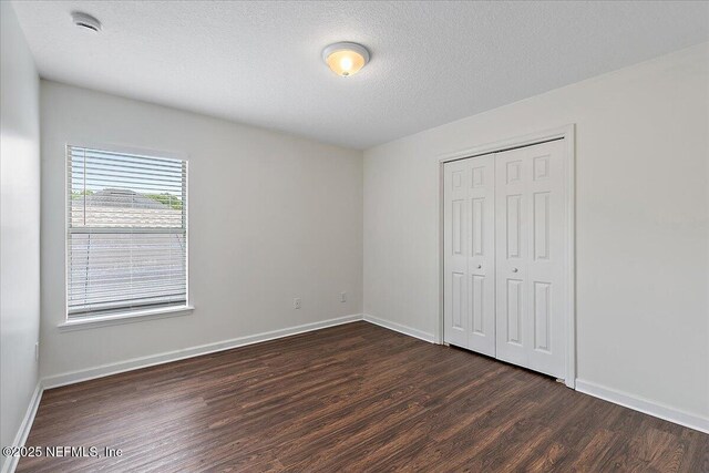 unfurnished bedroom with dark wood-style flooring, baseboards, a closet, and a textured ceiling