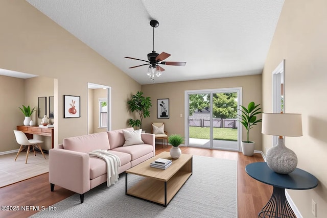 living room with lofted ceiling, a ceiling fan, wood finished floors, baseboards, and a textured ceiling