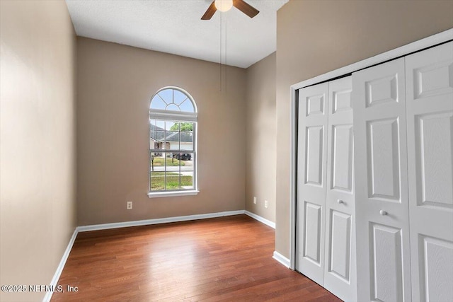 unfurnished bedroom featuring wood finished floors, baseboards, a closet, and a ceiling fan