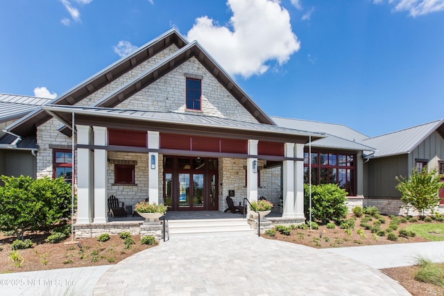 view of front of property featuring a standing seam roof, french doors, covered porch, and stone siding