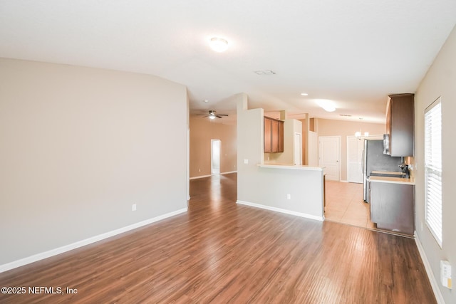 unfurnished living room featuring a chandelier, light wood finished floors, lofted ceiling, baseboards, and a ceiling fan