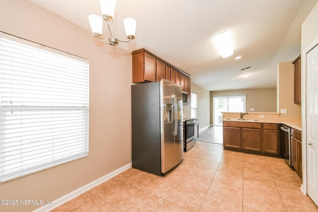 kitchen featuring stainless steel appliances, brown cabinetry, a sink, and baseboards