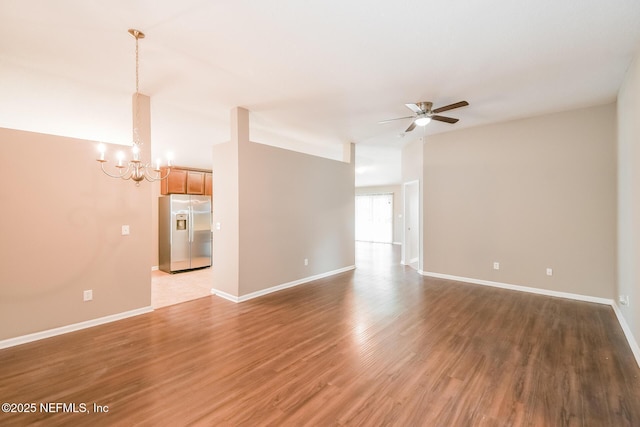 unfurnished living room featuring a chandelier, ceiling fan, wood finished floors, and baseboards