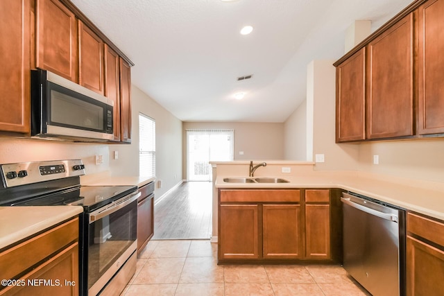 kitchen with appliances with stainless steel finishes, a peninsula, light countertops, a sink, and light tile patterned floors