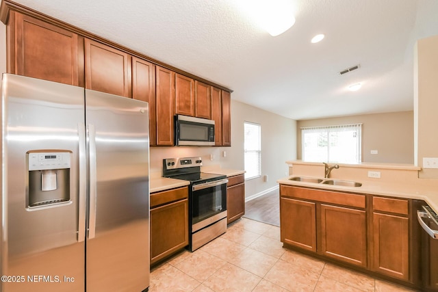 kitchen with stainless steel appliances, a sink, brown cabinetry, light countertops, and recessed lighting