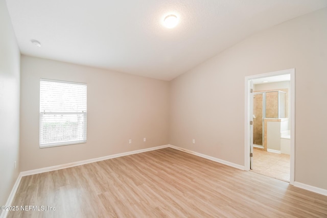 unfurnished room featuring light wood-style floors, lofted ceiling, a smoke detector, and baseboards