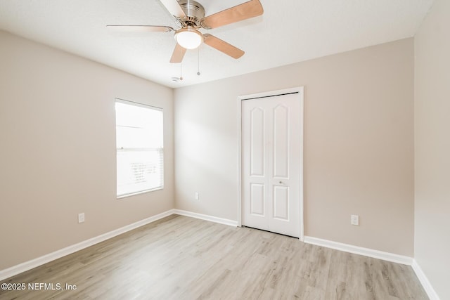 unfurnished bedroom featuring light wood-style floors, a closet, baseboards, and a ceiling fan