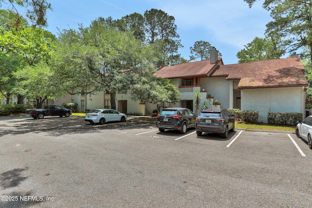1303 Wood Hill Pl Unit 1303, Jacksonville, FL 32256 - view of property featuring uncovered parking, stucco siding, a chimney, and roof with shingles