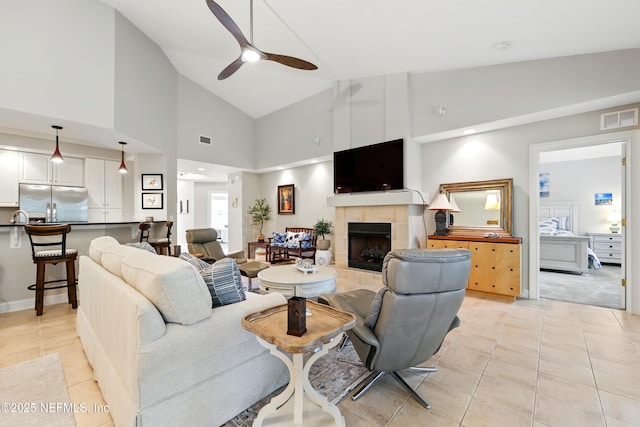 living area with light tile patterned flooring, a ceiling fan, a tile fireplace, and high vaulted ceiling
