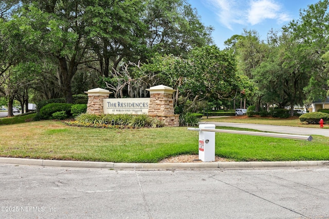 community sign with a lawn and view of scattered trees