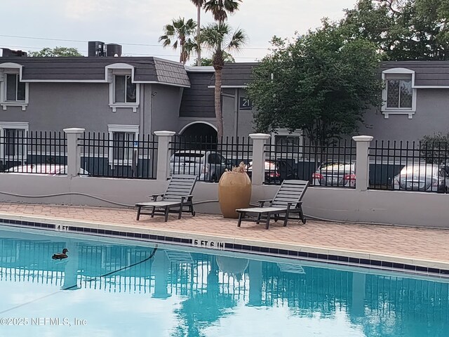 community pool featuring fence, central AC unit, and a patio area