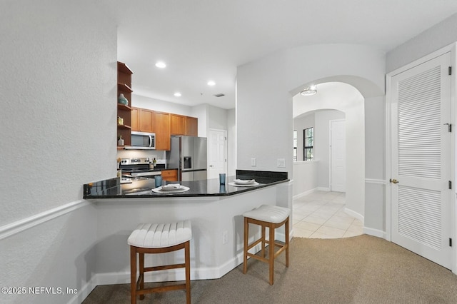 200 Paseo Terraza Unit 203, Saint Augustine, FL 32095 - kitchen featuring appliances with stainless steel finishes, arched walkways, open shelves, brown cabinets, and a kitchen breakfast bar