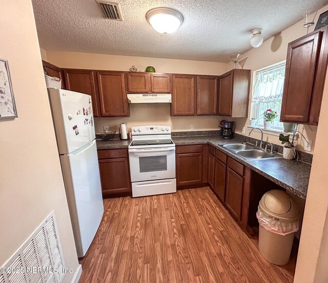 kitchen featuring white appliances, a sink, under cabinet range hood, dark countertops, and a textured ceiling