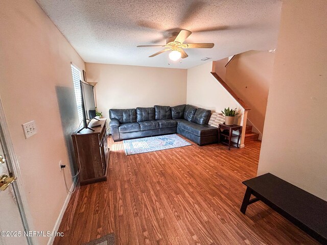 living area with wood finished floors, a ceiling fan, a textured ceiling, stairway, and baseboards