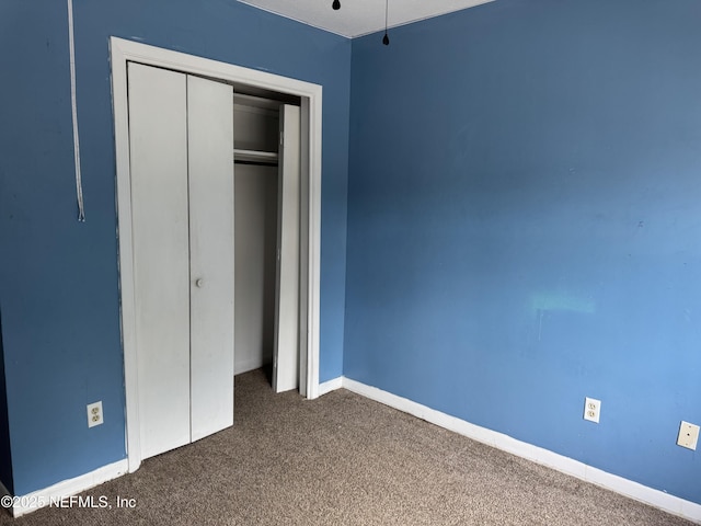 unfurnished bedroom with dark colored carpet, a closet, and baseboards