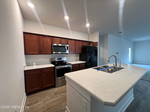 kitchen with appliances with stainless steel finishes, a sink, light wood finished floors, an island with sink, and light countertops