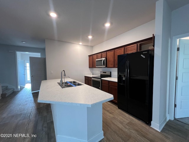 kitchen with stainless steel appliances, a sink, dark wood-style floors, an island with sink, and light countertops