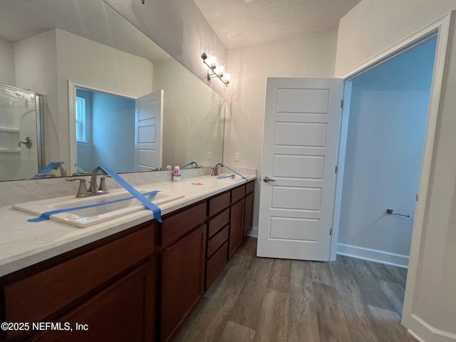 full bath featuring wood finished floors, a shower with shower door, double vanity, and a textured ceiling