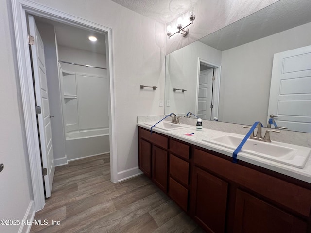 bathroom with wood finished floors, double vanity, baseboards, shower / bath combination, and a textured ceiling