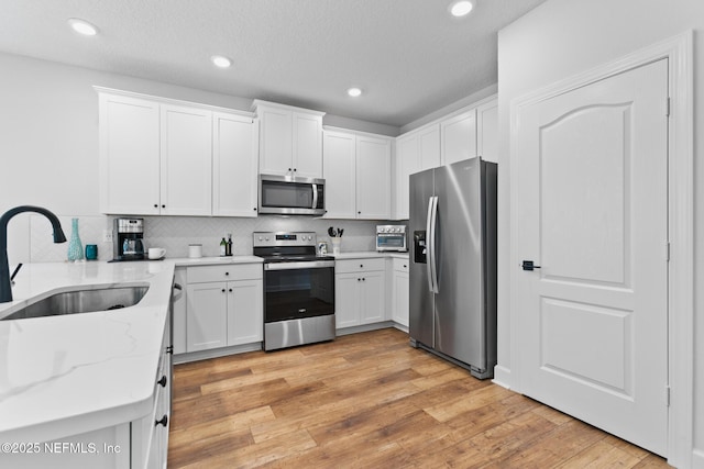 kitchen with stainless steel appliances, a sink, light stone counters, white cabinetry, and recessed lighting