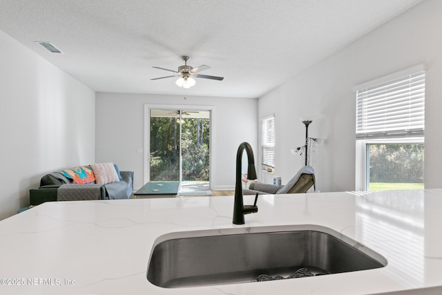 kitchen view of a sink, light stone countertops, ceiling fan, and a textured ceiling