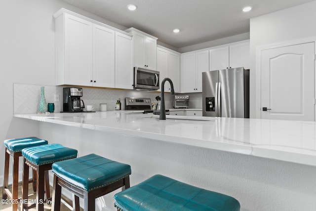 kitchen featuring stainless steel appliances, decorative backsplash, white cabinets, a kitchen bar, and recessed lighting