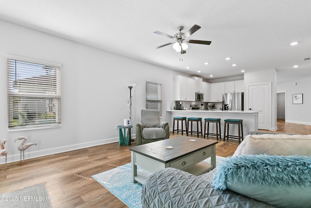 living room with ceiling fan, baseboards, recessed lighting, light wood finished floors, and a textured ceiling
