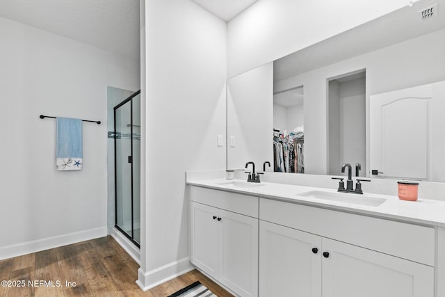bathroom featuring a stall shower, wood finished floors, a walk in closet, and baseboards