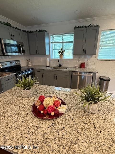 6845 Cherbourg Ave S, Jacksonville, FL 32205 - kitchen featuring stainless steel appliances, a sink, ornamental molding, backsplash, and light stone countertops