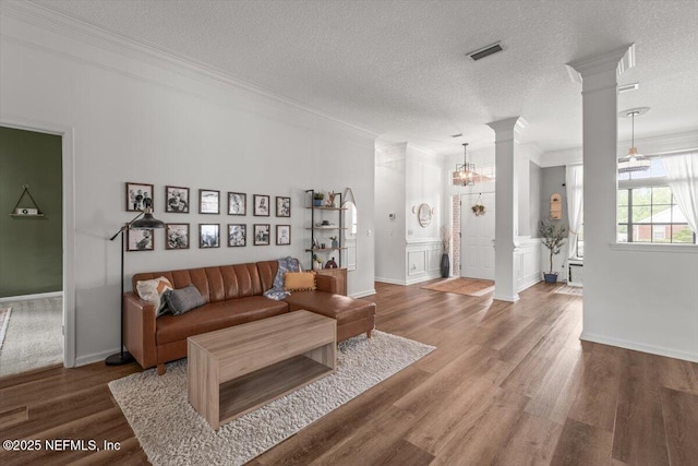 living area featuring ornamental molding, decorative columns, wood finished floors, and a textured ceiling