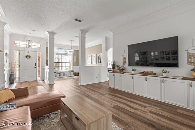 living room with decorative columns, crown molding, wood finished floors, a chandelier, and a textured ceiling