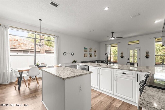 kitchen featuring a kitchen island, a sink, light wood-style floors, a ceiling fan, and a textured ceiling
