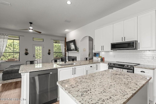 kitchen with stainless steel appliances, open floor plan, a peninsula, a sink, and arched walkways