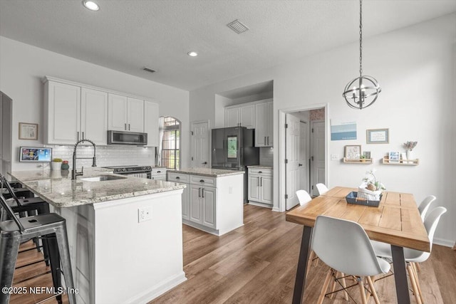 kitchen with appliances with stainless steel finishes, a peninsula, a chandelier, a sink, and tasteful backsplash