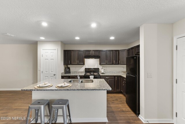 1343 Pangola Dr, Jacksonville, FL 32205 - kitchen featuring black appliances, dark brown cabinets, a textured ceiling, a kitchen island with sink, and under cabinet range hood