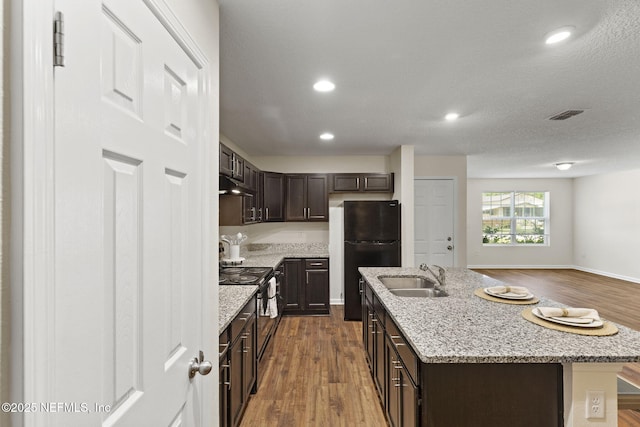 1343 Pangola Dr, Jacksonville, FL 32205 - kitchen featuring black appliances, under cabinet range hood, dark brown cabinets, dark wood finished floors, and a kitchen island with sink