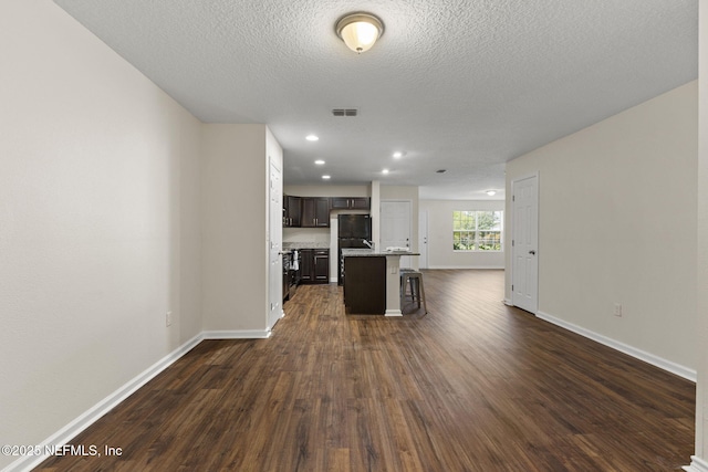 1343 Pangola Dr, Jacksonville, FL 32205 - kitchen featuring dark wood finished floors, a breakfast bar, an island with sink, a textured ceiling, and dark brown cabinetry