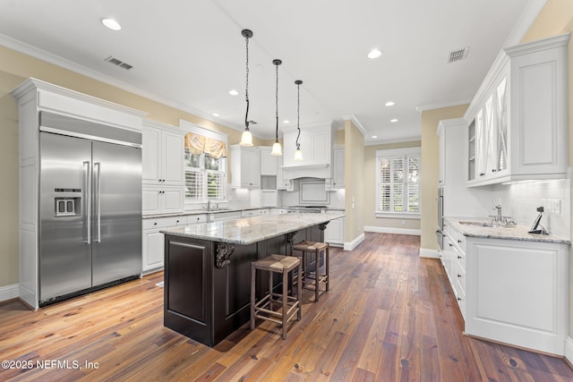 kitchen with stainless steel appliances, a sink, a kitchen island, ornamental molding, and white cabinets